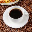 side view of a cup of coffee with wafer roll filled with condensed milk on a plate on coffee beans background